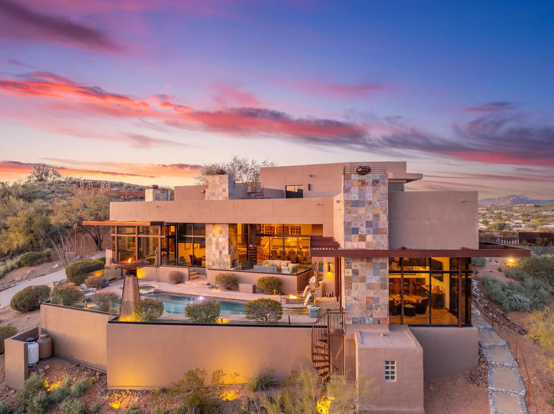 Dusk aerial of the lit Saguaro Point estate, pool, and fire features
