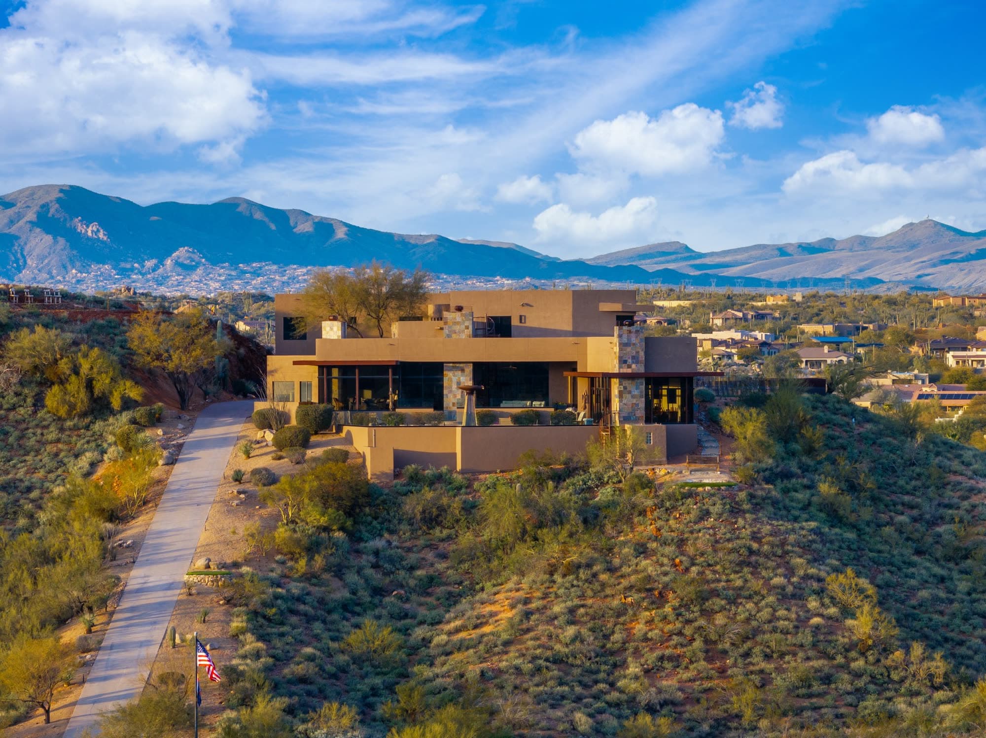 The front of the Saguaro Point estate on its ridge, driveway and flagpole leading in, mountains behind
