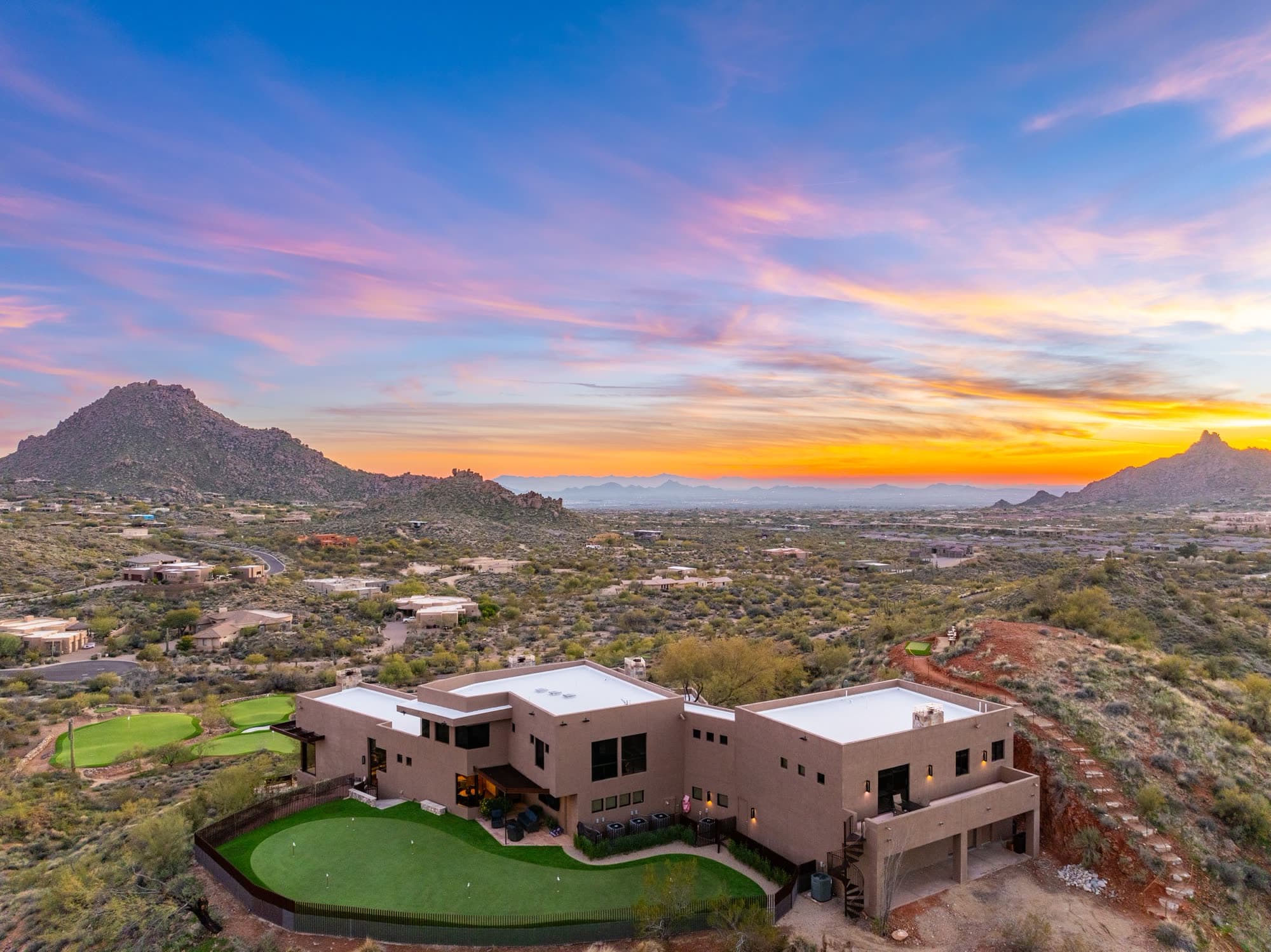 Wide dusk view of the rear of the Saguaro Point house at right, the greens at left, and the sunset beyond