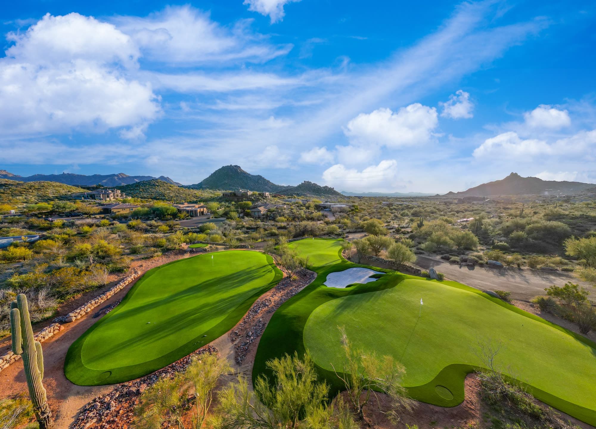 Two large putting greens in the foreground with a saguaro at left and the North Scottsdale mountains behind